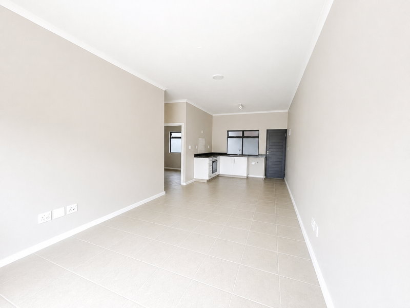 An open-plan living and kitchen area featuring neutral tiled flooring, modern cabinetry with dark countertops, and a clean, minimalist aesthetic.