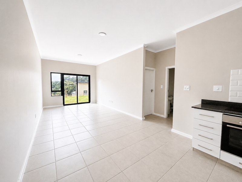 Bright open-plan living area featuring tiled floors, a modern kitchen with granite countertops, and sliding glass doors leading to an outdoor view.