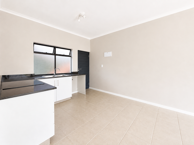 A clean, empty kitchen featuring neutral tiled floors, white cabinetry, granite countertops, and a stainless steel sink with a window view.