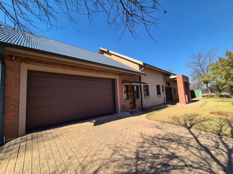 Front exterior view of the house featuring a paved driveway, brick facade, and a large automated garage door under a metal roof.