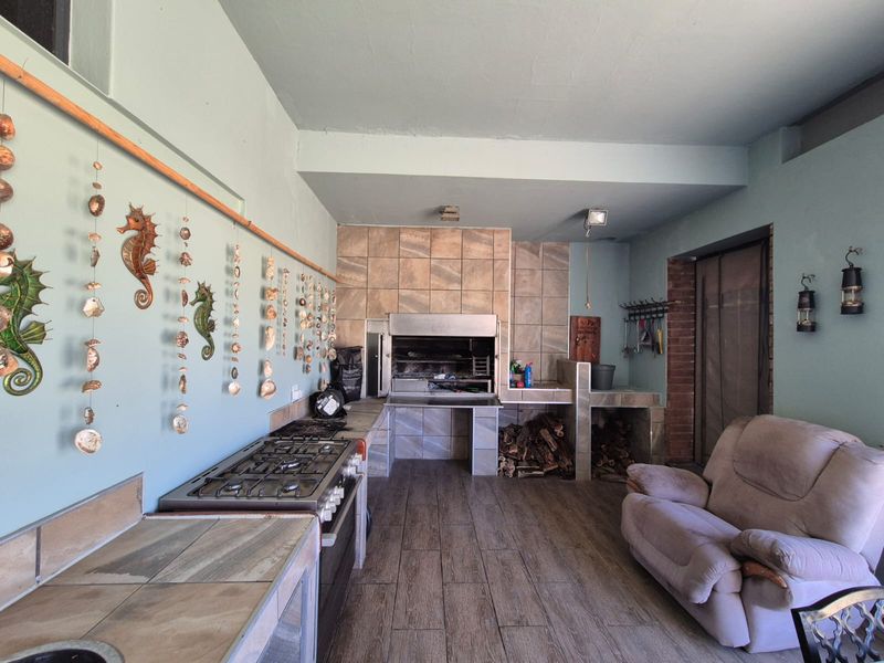 Covered patio area featuring a built-in braai, gas hob, and tiled flooring, offering a functional space for outdoor cooking and entertainment.