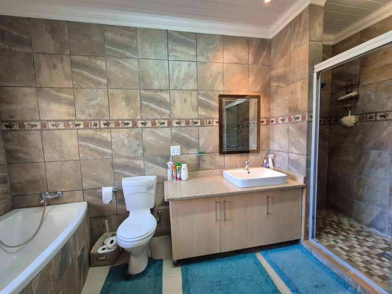 A functional bathroom featuring a built-in vanity with countertop basin, a separate bathtub, and a glass-enclosed shower with full-height wall tiling.