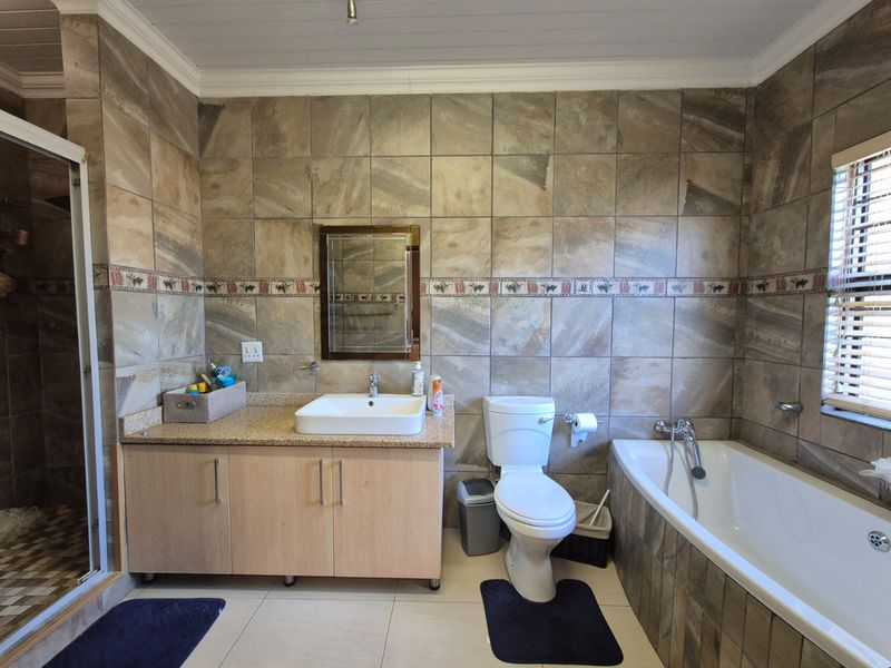 A functional bathroom featuring a vanity with vessel sink, a bathtub, a separate shower enclosure, and full-height wall tiling.
