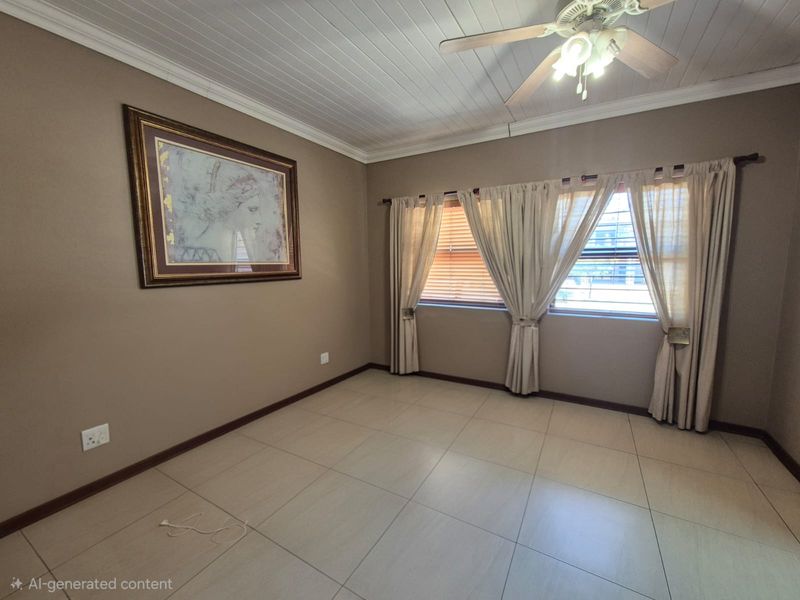 A spacious, empty bedroom featuring tiled flooring, a tongue and groove ceiling with a fan, and large windows with fitted blinds.