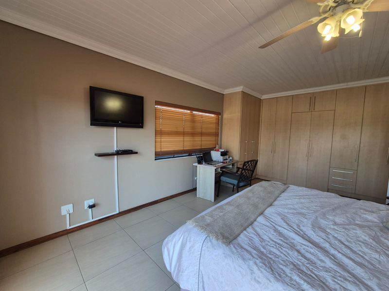 Spacious bedroom featuring extensive built-in cabinetry, tiled flooring, a ceiling fan, and large windows with venetian blinds.