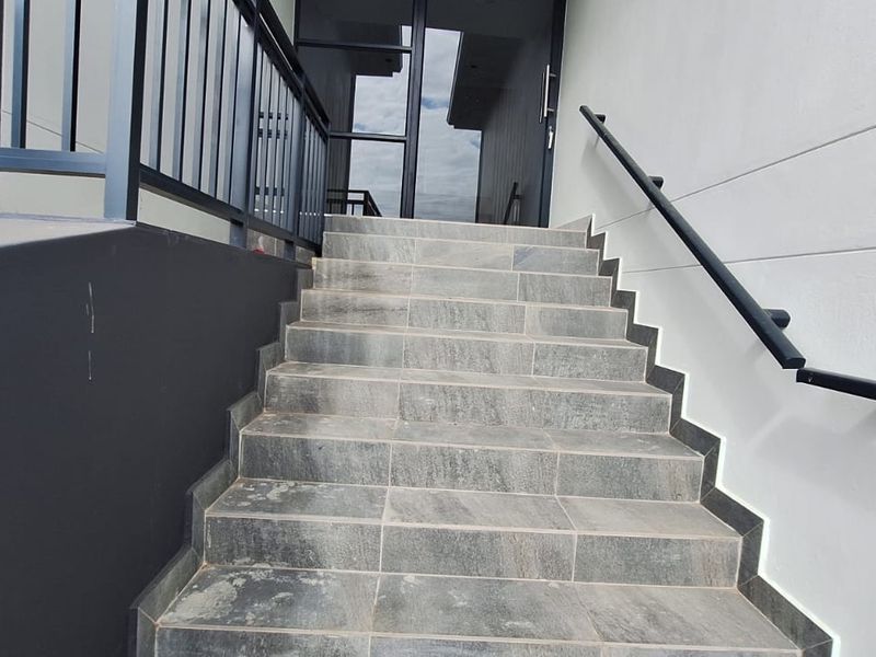 A modern exterior entrance featuring a tiled staircase with a sleek metal handrail leading up to a glass front door.