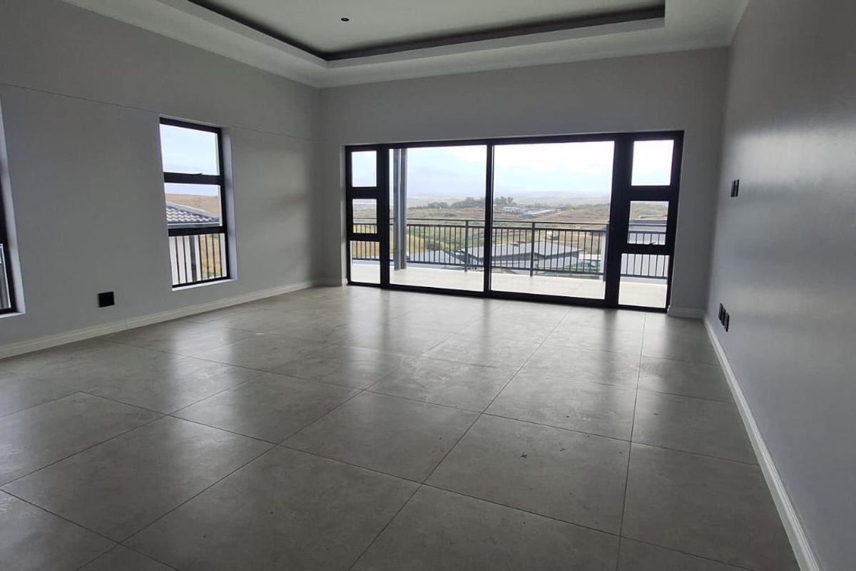 Spacious, modern living area featuring large format floor tiles, recessed ceiling detail, and expansive sliding doors leading to a balcony with scenic views.