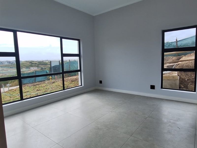 A bright, empty bedroom featuring large aluminium-framed windows with scenic views and modern neutral floor tiles.