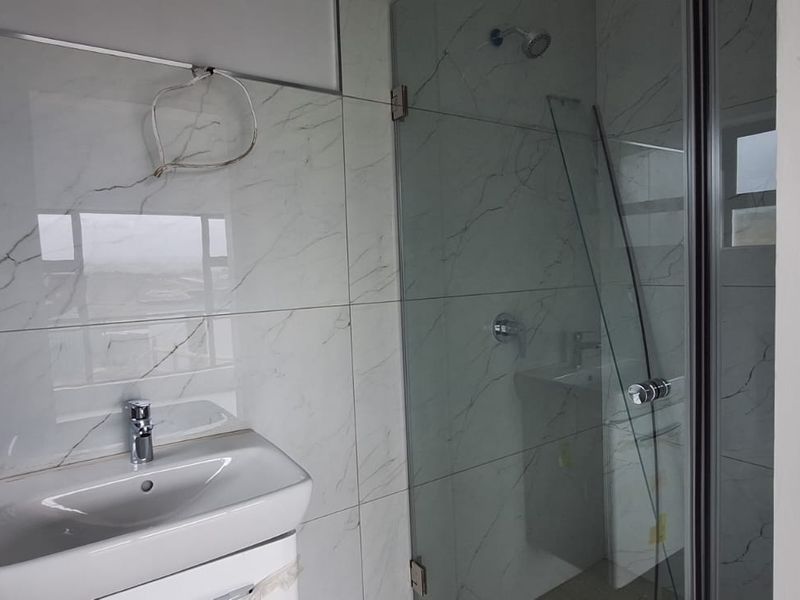 A modern bathroom featuring marble-look wall tiles, a wall-mounted vanity basin, and a glass-enclosed shower, currently requiring minor finishing touches.