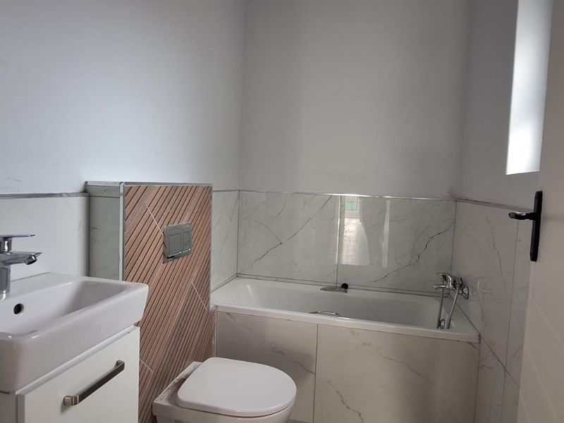 A modern, clean bathroom featuring a vanity basin, wall-hung toilet with concealed cistern, and a bathtub with marble-look wall tiling.