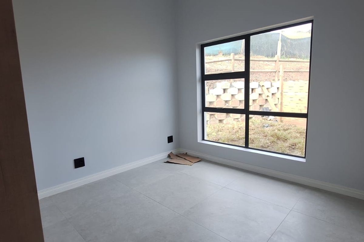 A bright, empty bedroom featuring modern large-format floor tiles, neutral wall paint, and a large aluminium-framed window overlooking the rear yard.