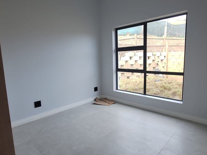 A bright, empty bedroom featuring modern large-format floor tiles, neutral wall paint, and a large aluminium-framed window overlooking the rear yard.