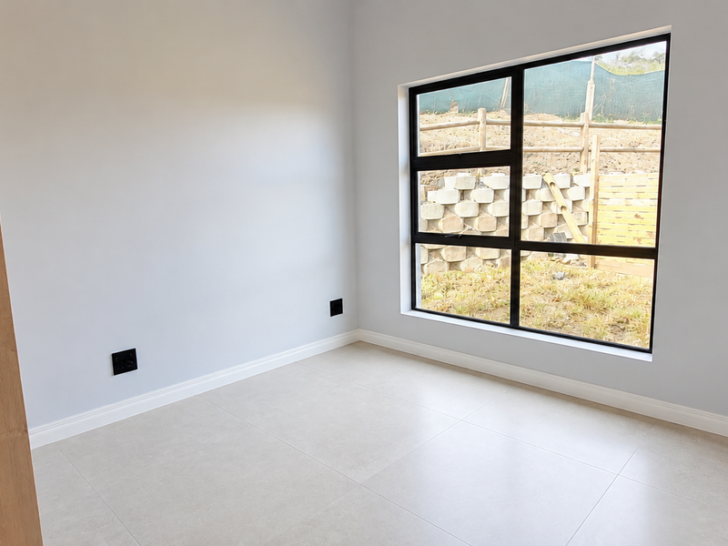 A bright, modern, and empty bedroom featuring neutral tiled flooring, clean white walls, and a large window overlooking the rear garden area.