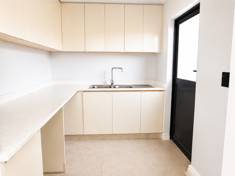 A clean, modern scullery featuring ample built-in cabinetry, stone countertops, a stainless steel sink, and direct access to the exterior.