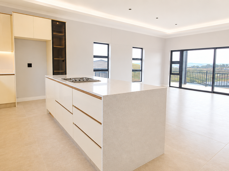 Spacious open-plan kitchen and living area featuring a modern island, high-gloss cabinetry, stone countertops, and large sliding doors leading to a balcony with views.