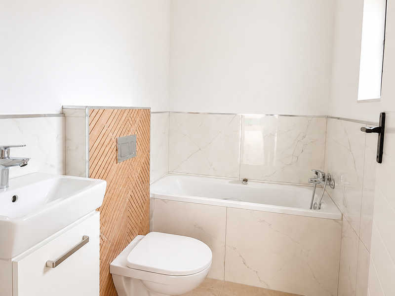 A modern, clean bathroom featuring a wall-mounted toilet, vanity basin, and bathtub with marble-look wall tiling and contemporary chrome fixtures.