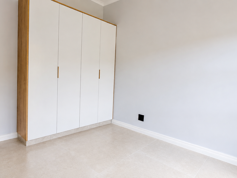 A bright, modern bedroom featuring neutral tiled flooring, crisp white walls, and a sleek, contemporary built-in wardrobe with wood-grain detailing.