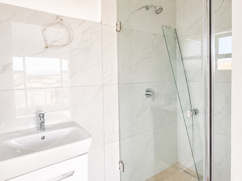 Modern bathroom featuring a wall-mounted vanity with basin, marble-look wall tiling, and a glass-enclosed shower with chrome fixtures.