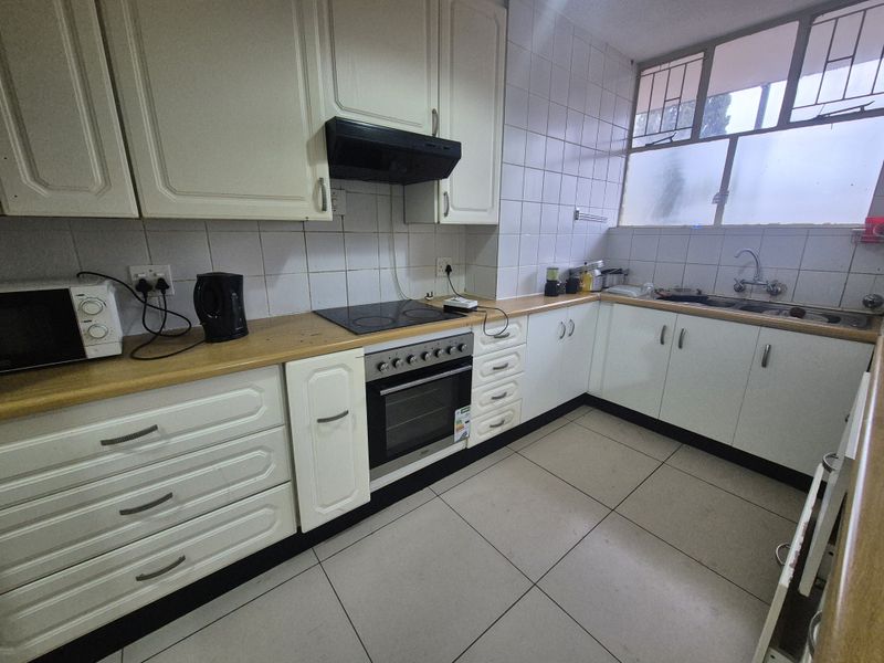 Functional kitchen featuring white cabinetry, electric hob, built-in oven, extractor fan, and tiled flooring with ample counter space.