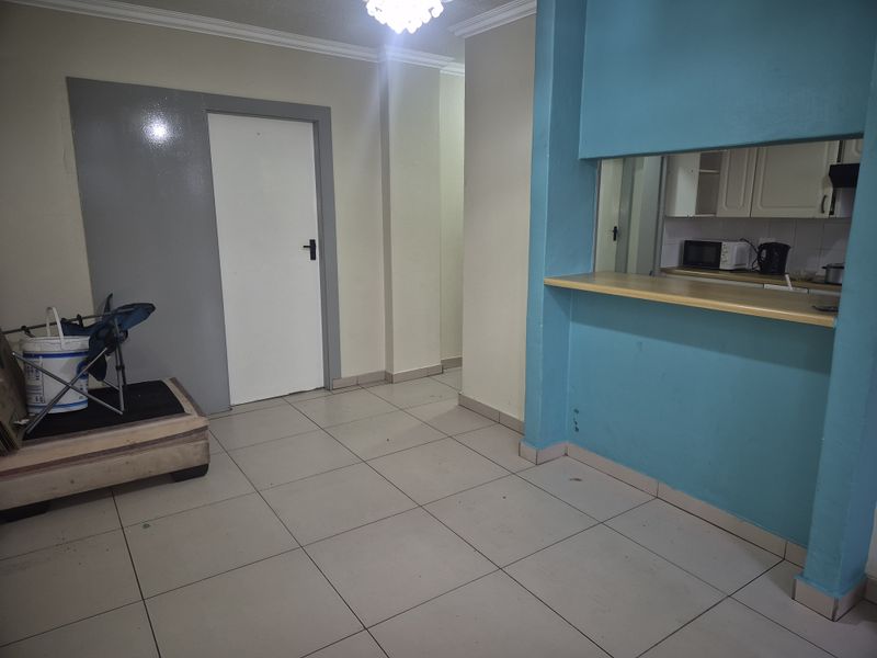 Open plan living area featuring tiled flooring and a breakfast bar pass-through to the kitchen, offering a functional layout ready for modernization.