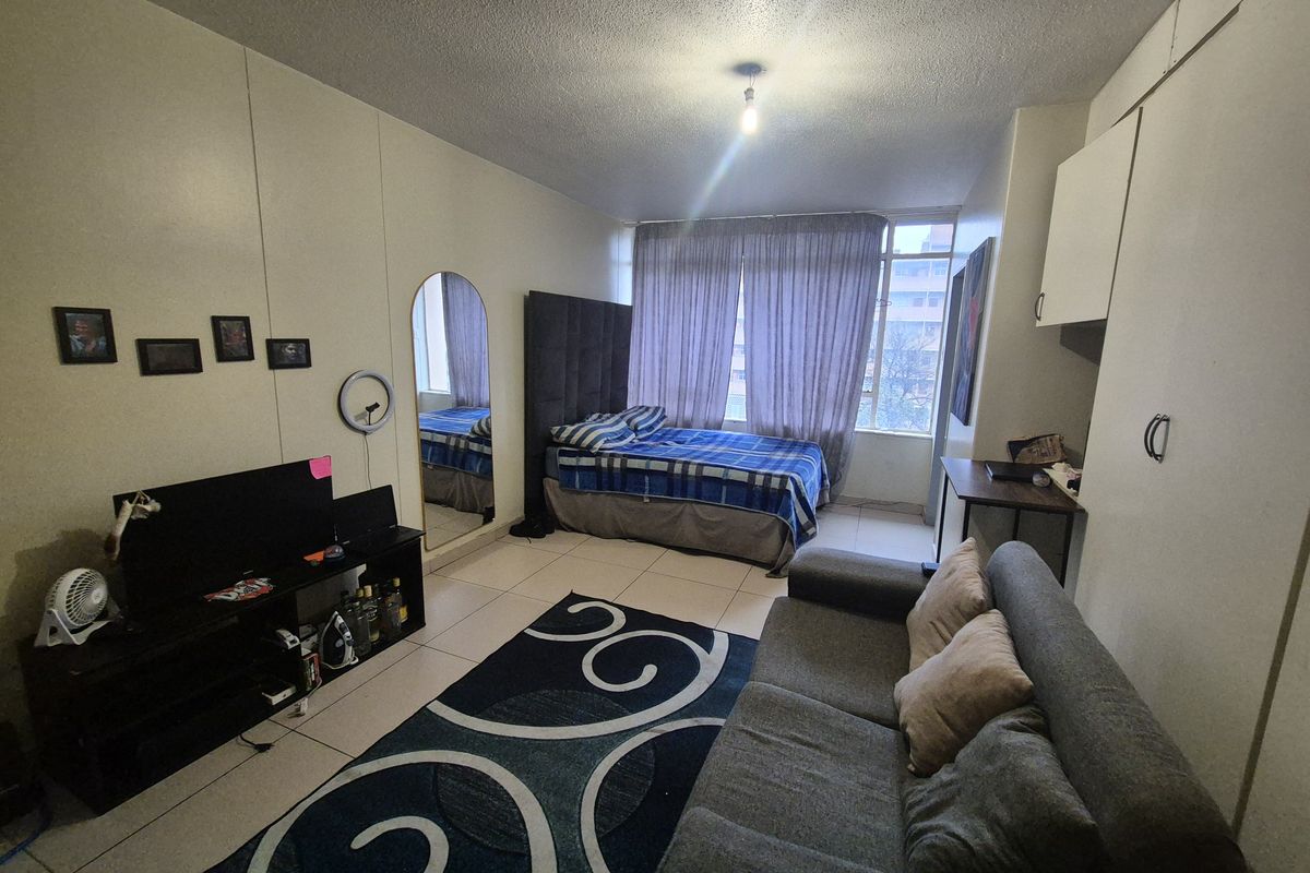 Open-plan studio apartment featuring tiled flooring, built-in storage cupboards, and large windows allowing natural light.