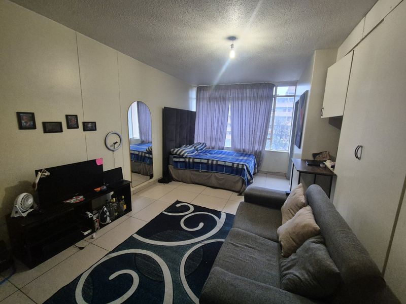 Open-plan studio apartment featuring tiled flooring, built-in storage cupboards, and large windows allowing natural light.