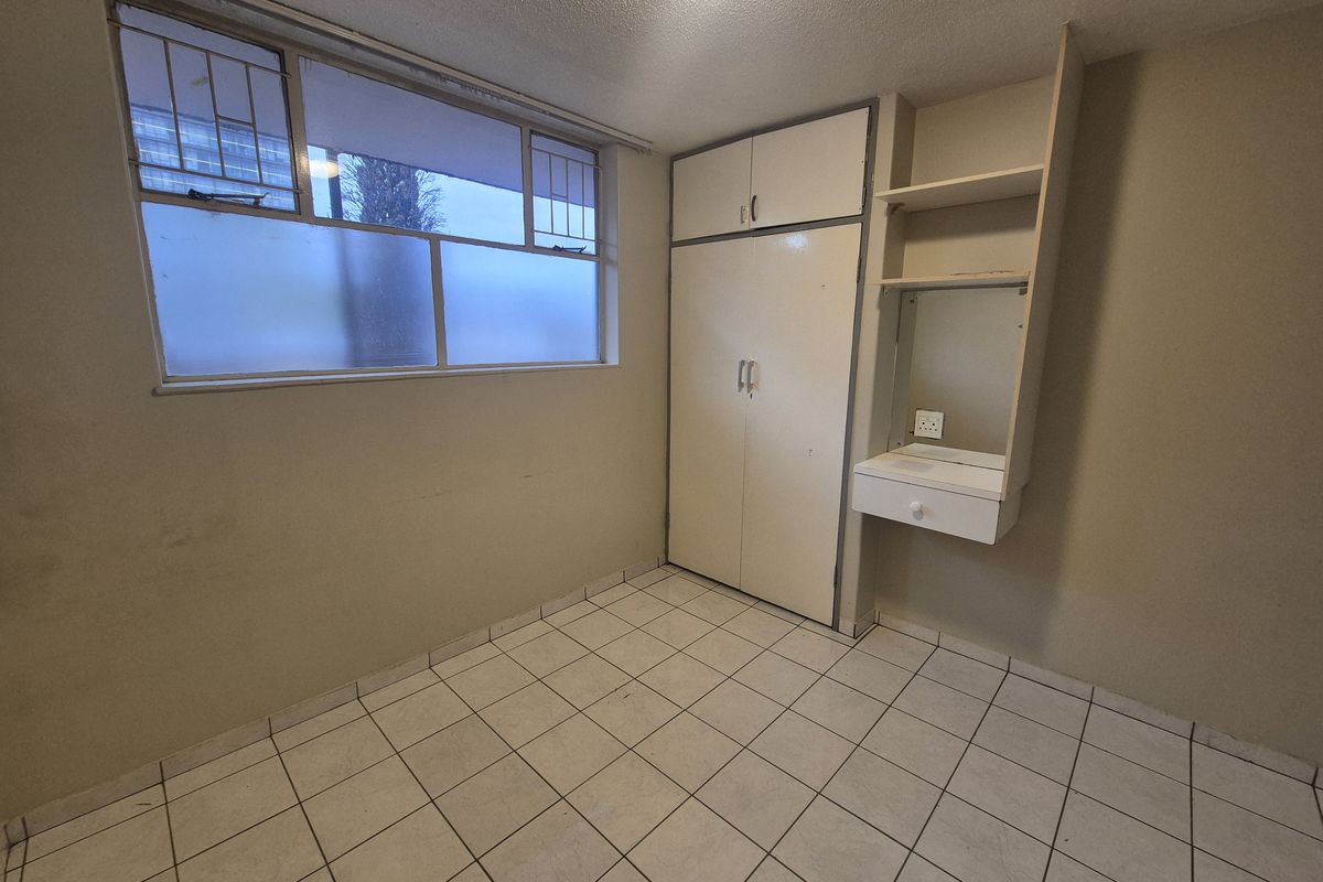 An empty bedroom featuring tiled flooring, a built-in wardrobe, and a built-in vanity unit with shelving.