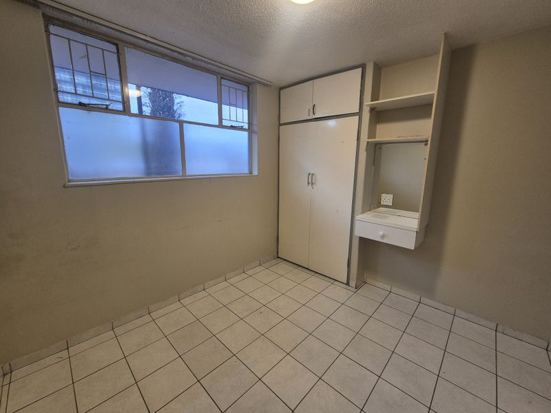 An empty bedroom featuring tiled flooring, a built-in wardrobe, and a built-in vanity unit with shelving.