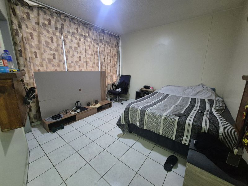A bedroom featuring tiled flooring and a large window covered by curtains.