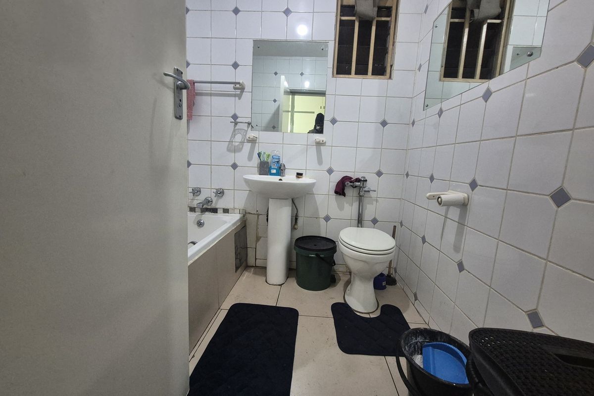 A compact bathroom featuring a pedestal basin, toilet, and bathtub with tiled walls and flooring, requiring some maintenance and cosmetic updates.