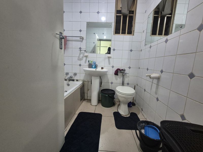A compact bathroom featuring a pedestal basin, toilet, and bathtub with tiled walls and flooring, requiring some maintenance and cosmetic updates.