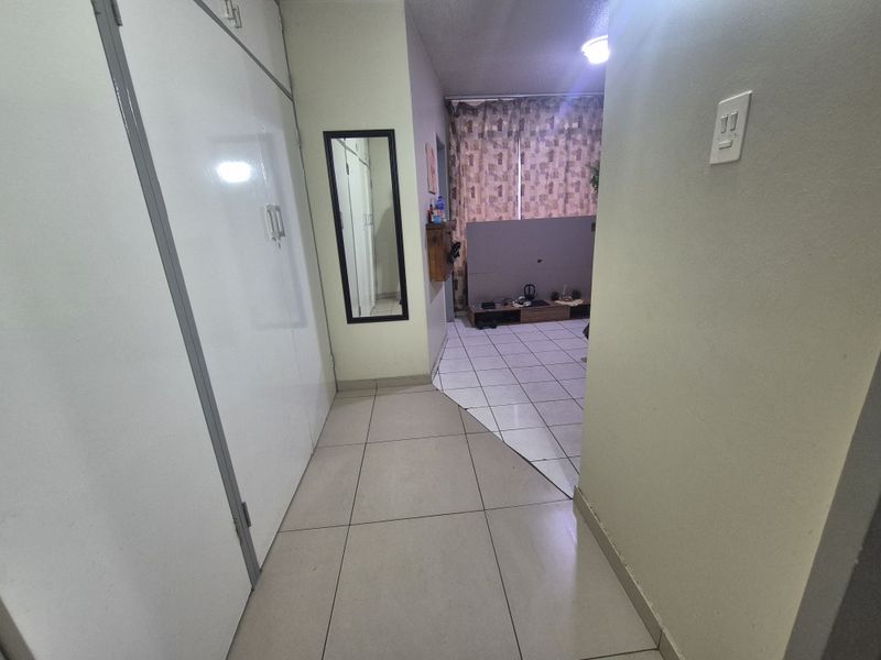A functional hallway featuring built-in storage cupboards and ceramic floor tiles, leading into the main living area of the apartment.
