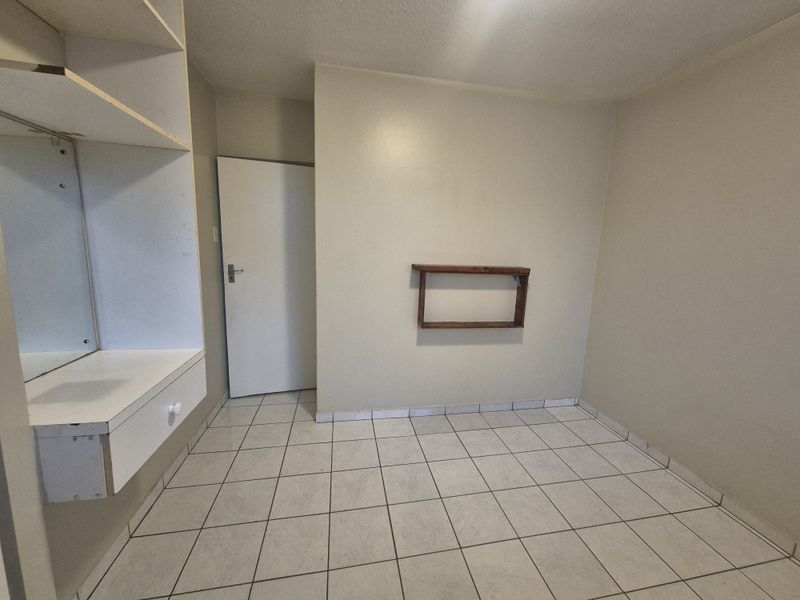 An empty bedroom featuring tiled flooring, a built-in vanity unit, and a wall-mounted shelf, offering a blank canvas for personalization.