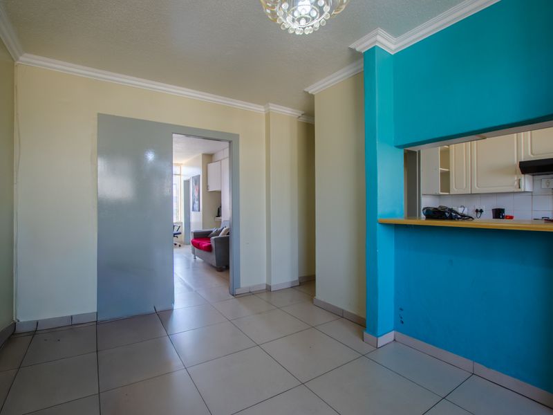 Open plan living area featuring tiled flooring, a breakfast bar pass-through to the kitchen, and neutral wall finishes with decorative coving.