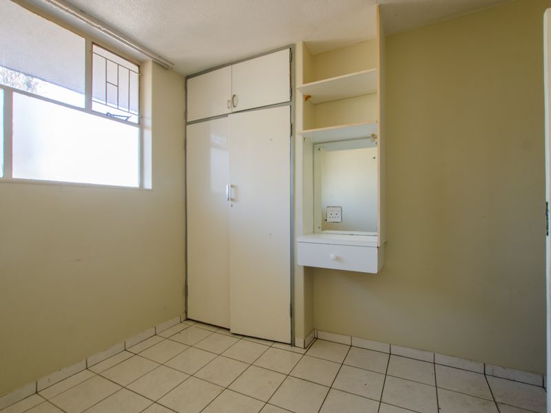 A vacant bedroom featuring tiled flooring, a built-in wardrobe, and a small integrated vanity unit with a mirror.