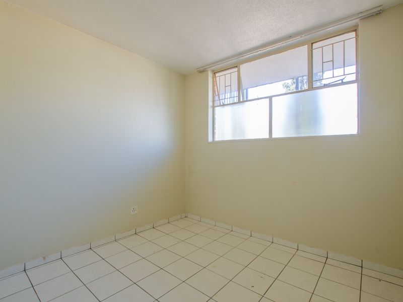 An empty bedroom featuring tiled flooring, neutral walls, and a window fitted with security bars.