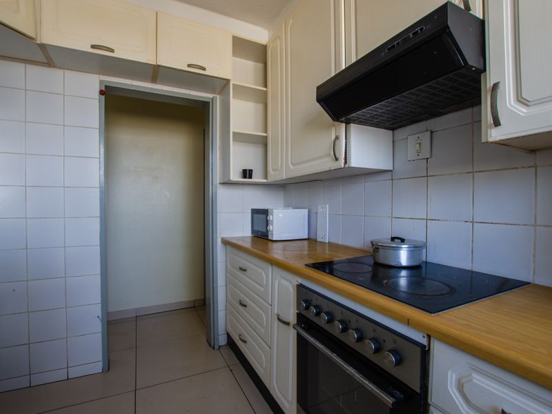 A functional kitchen featuring built-in cabinetry, an electric hob with extractor fan, and tiled backsplash, offering a practical layout for daily cooking.