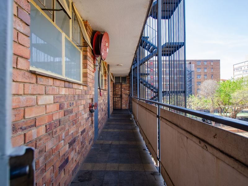An exterior apartment balcony featuring brick walls, a fire hose reel, and a metal fire escape staircase overlooking the surrounding neighborhood.