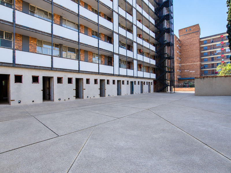 A view of the rear exterior of a multi-story apartment building featuring a large concrete paved courtyard and an external fire escape staircase.