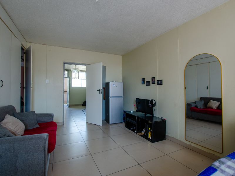 A living room area featuring tiled flooring and built-in storage cupboards, providing a functional space with direct access to an adjacent room.