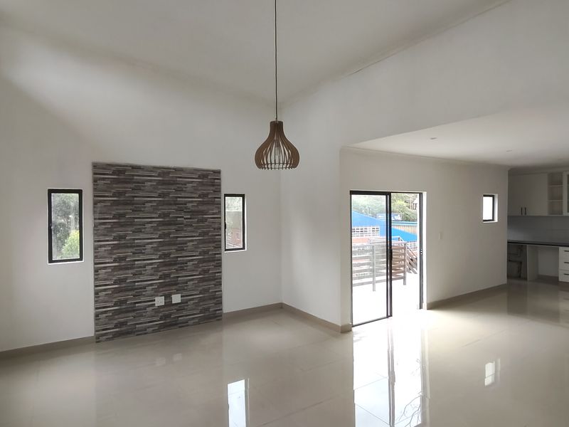 Spacious open-plan living and kitchen area featuring polished tile floors, a stone feature wall, and modern built-in cabinetry with integrated appliances.