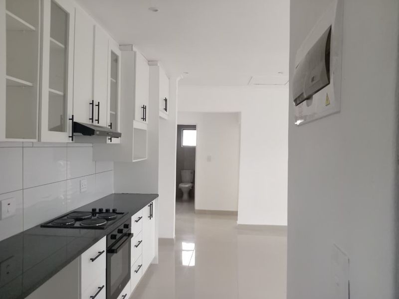 Modern kitchen featuring white cabinetry, dark countertops, integrated electric hob and oven, with tiled flooring and a view through to the bathroom.