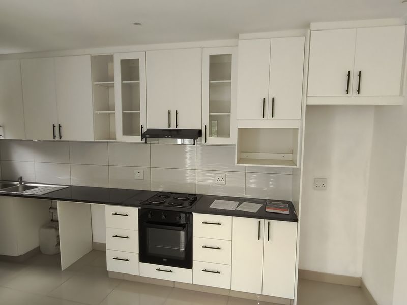 A clean, modern kitchen featuring white cabinetry, dark countertops, integrated oven and hob, and tiled backsplash in a bright, open-plan layout.