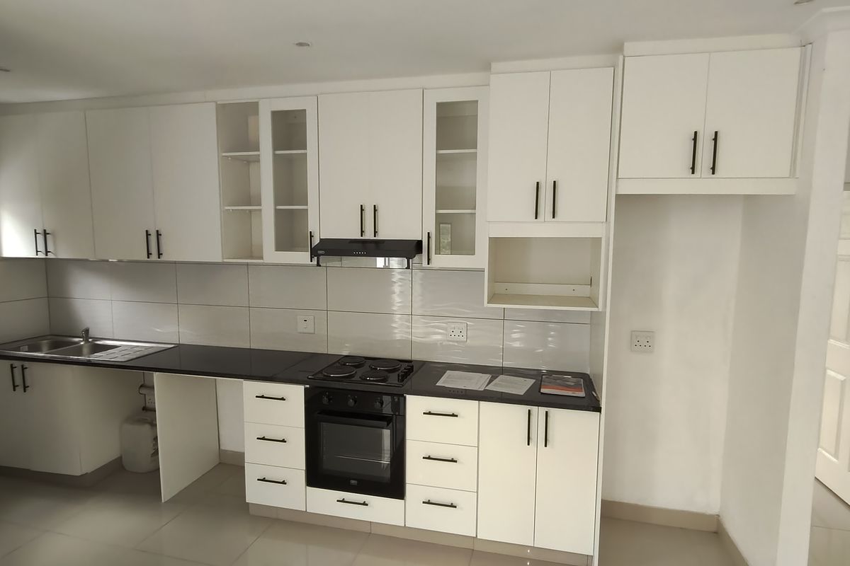 A clean, modern kitchen featuring white cabinetry, dark countertops, integrated oven and hob, and tiled backsplash in a bright, open-plan layout.