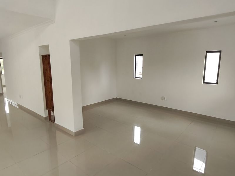 A spacious, empty open-plan living area featuring neutral tiled flooring, recessed lighting, and clean white walls, offering a versatile blank canvas.