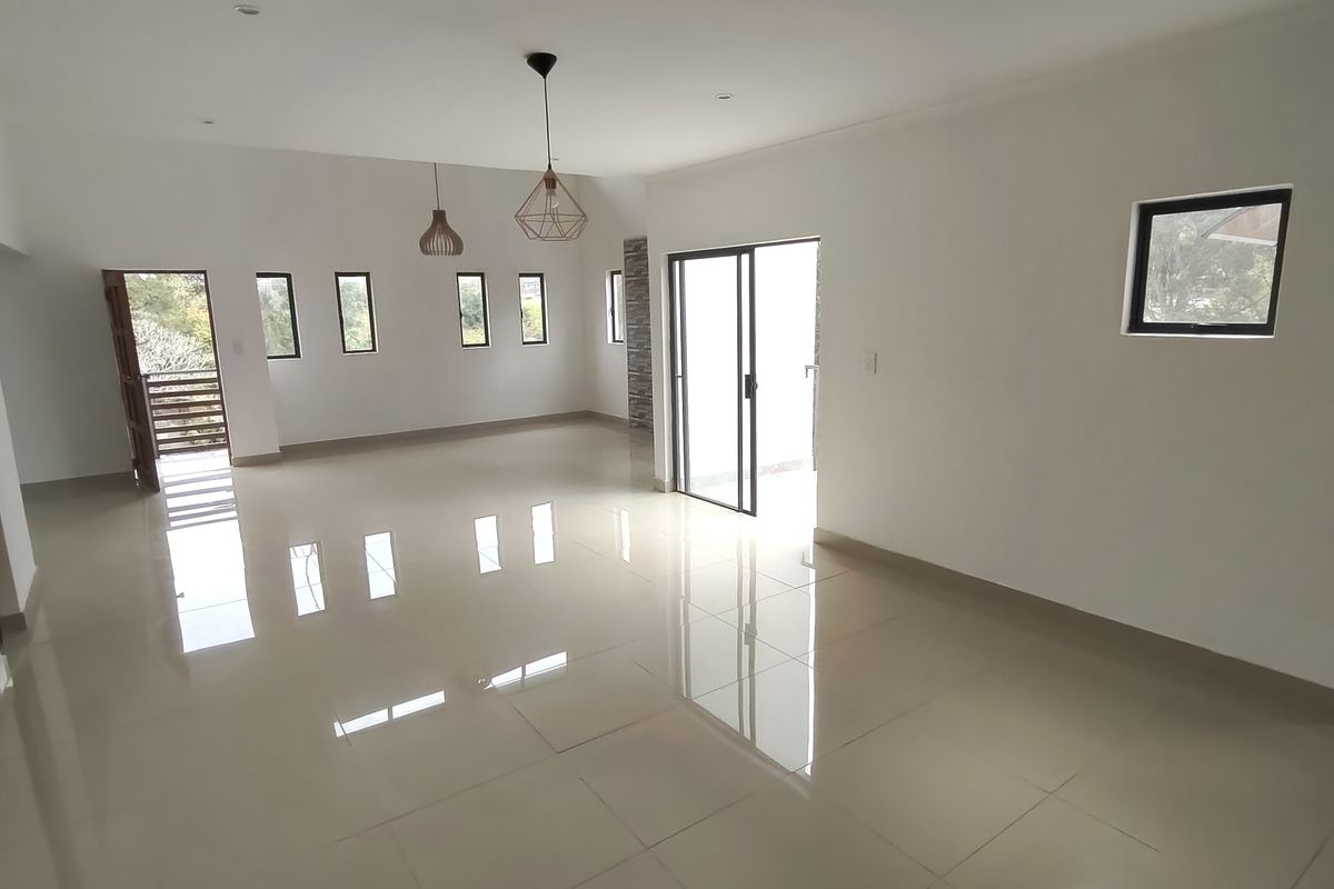 A spacious, bright, and empty living area featuring polished tiled floors, modern pendant lighting, and sliding glass doors leading to an outdoor space.