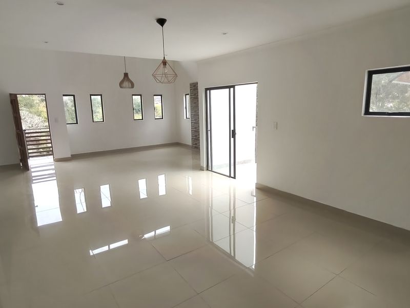 A spacious, bright, and empty living area featuring polished tiled floors, modern pendant lighting, and sliding glass doors leading to an outdoor space.