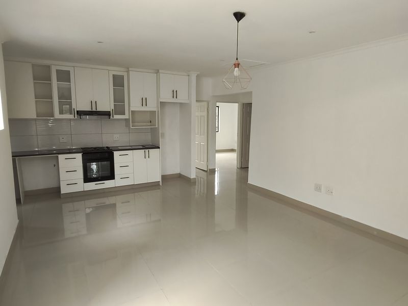 Spacious open-plan living area featuring a modern kitchen with built-in cabinetry, oven, hob, and extractor fan, finished with neutral tiled flooring.