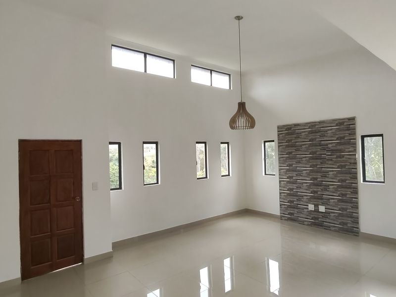 Spacious living area featuring high vaulted ceilings, clerestory windows for natural light, polished tile flooring, and a modern stone feature wall.
