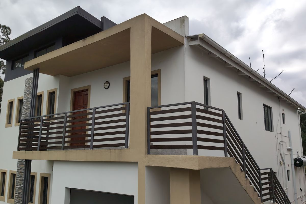 Rear exterior view of the townhouse featuring a balcony, external staircase with metal railings, and stone cladding accents.
